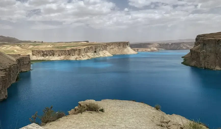 Dramatic cliffs surround the blue waters of Band-e Amir Lake under a cloudy sky in Afghanistan.